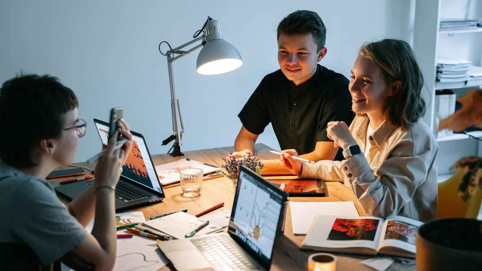 Three colleagues at a table with laptops and sketches reviewing design work together