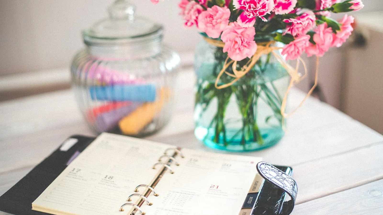 Open paper planner with dated pages beside a vase of pink carnations, tied to tracking days across a tax year