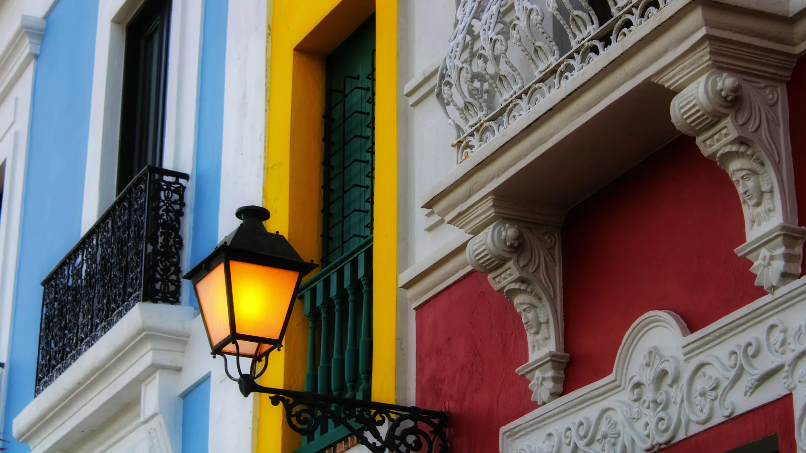 Blue, yellow and red painted facades with iron balconies and a lit street lamp, for a residency rules guide