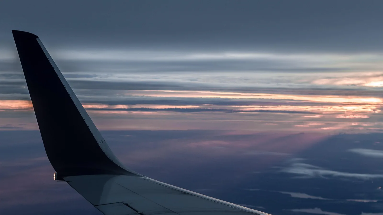 Airplane wing and winglet seen from a window at dusk, a travel day ending as the sky darkens
