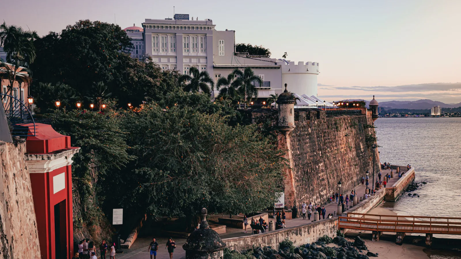 Old San Juan fortress wall and stone sentry box above the bay at dusk, with people walking the path below