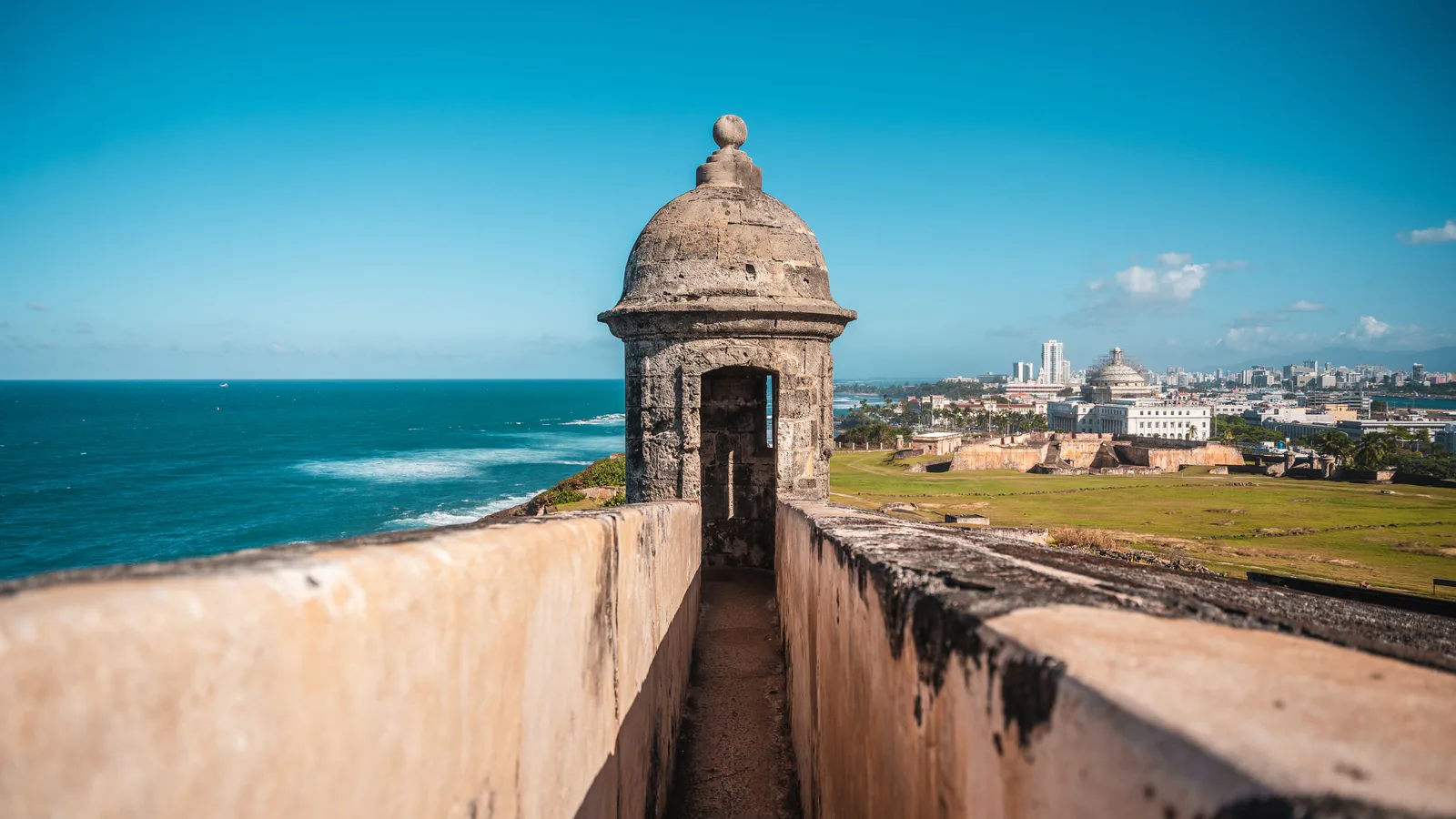 Stone sentry box on a San Juan fort wall, with the ocean on one side and the city skyline on the other