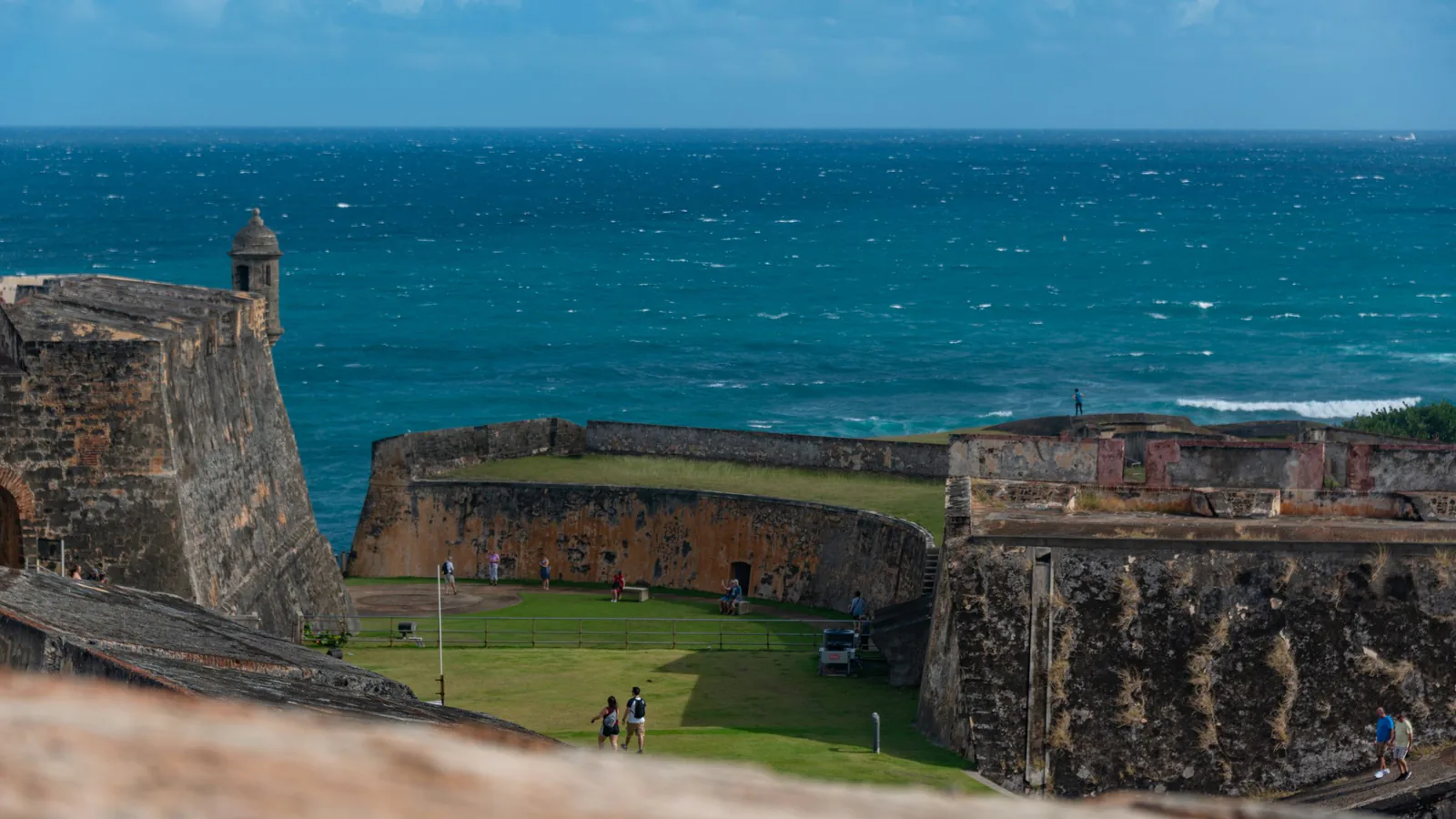 Stone fort walls and a sentry turret above a green courtyard, with the blue Atlantic beyond in Puerto Rico