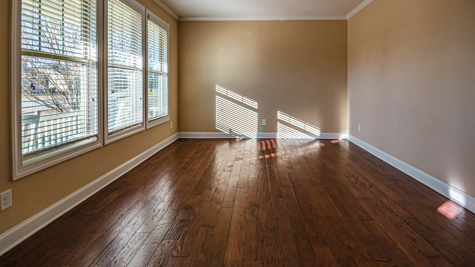 Empty room with dark hardwood floors and sunlight through window blinds, suggesting a vacant home