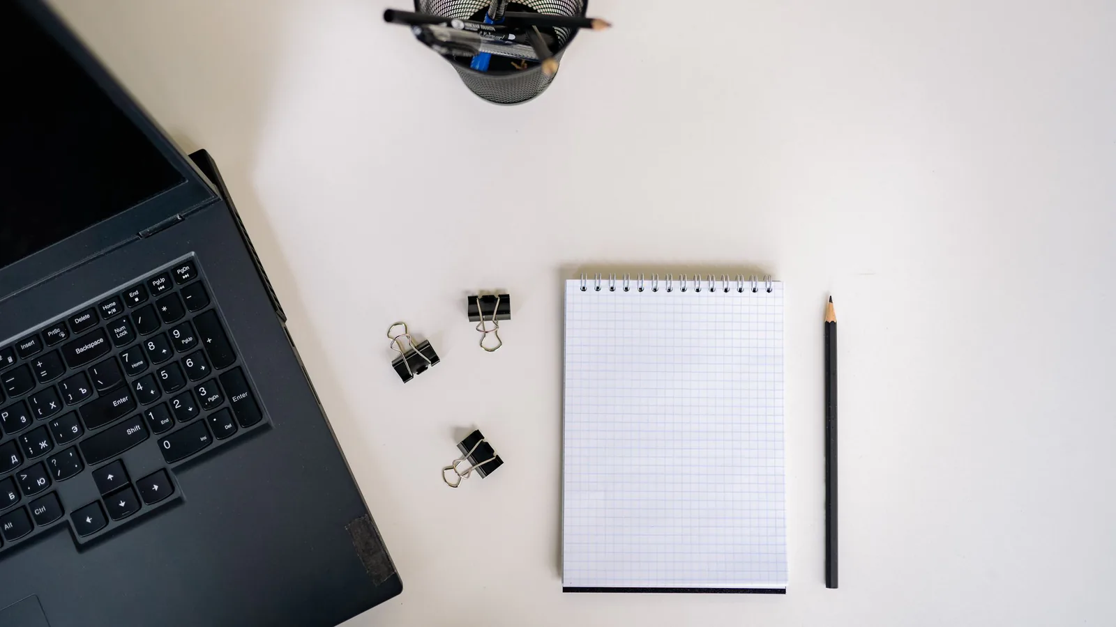 Blank grid notepad, pencil and binder clips beside a laptop on a white desk, a planning space for a mid-year move