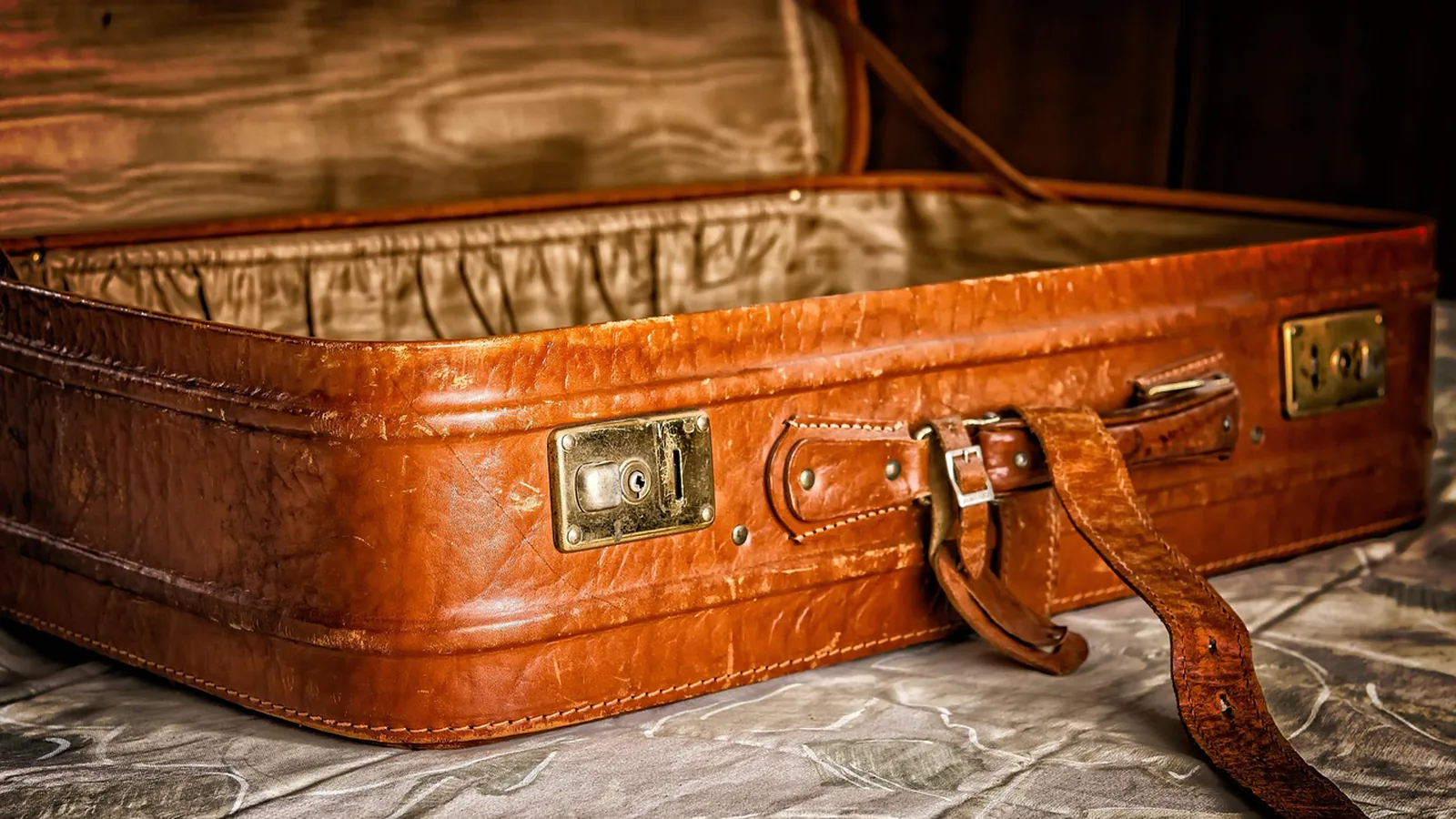 Open brown leather suitcase with brass latches on a bed, tied to the idea of where a permanent home is
