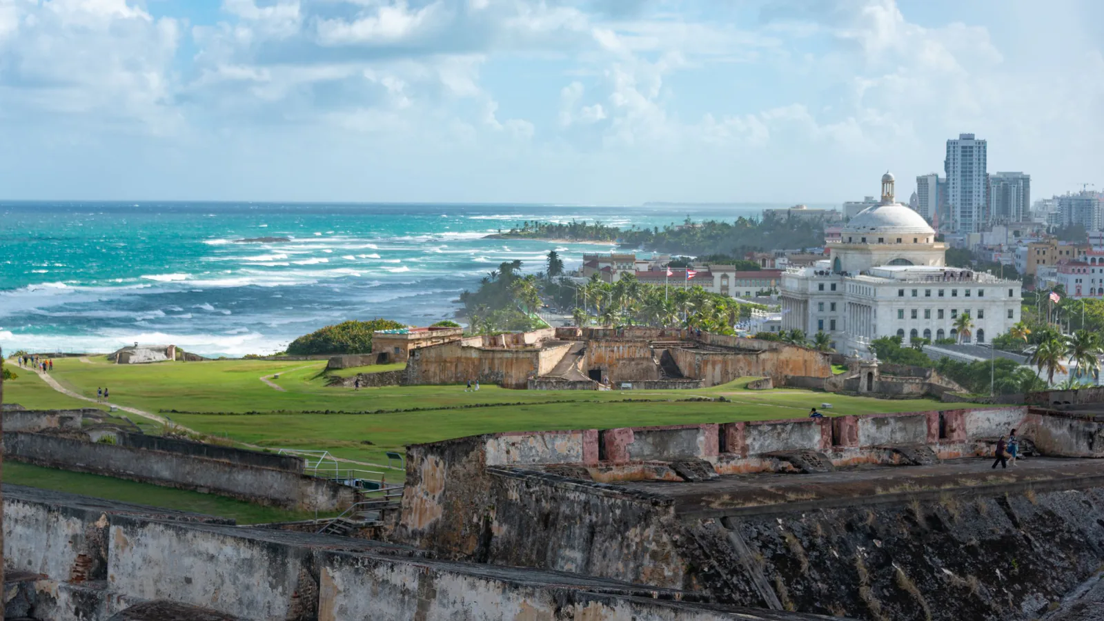 Historic stone walls and green lawn overlooking the turquoise coast and skyline of San Juan, Puerto Rico