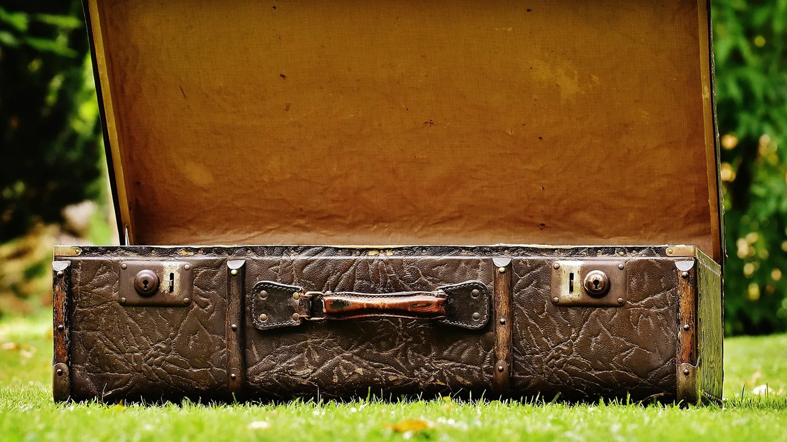 Open worn leather suitcase resting on green grass, a nod to the luggage flight crew carry between layovers