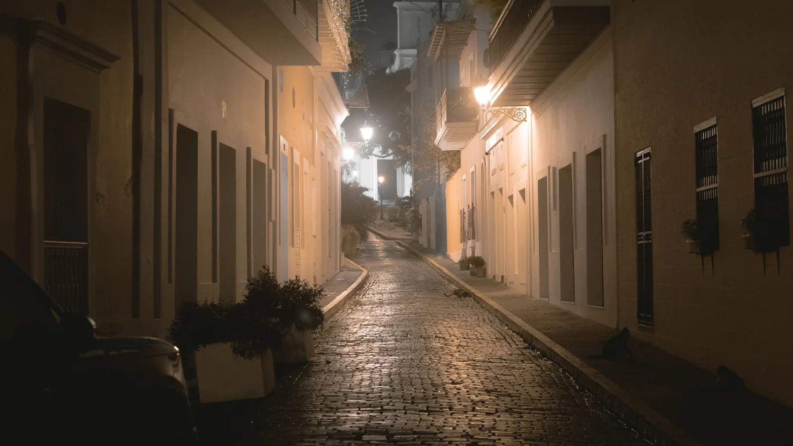 Empty cobblestone street at night with warm lamplight and balconied buildings, evoking time away from home